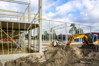 Yeni bir modern fabrikanın inşaat sahası beton ve metal yapı iskeletini güçlendirdi, kazıcılı toprak çalışmaları, kazma kazma kazıları