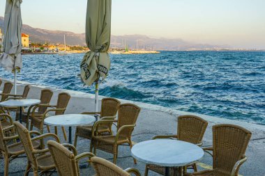 Sezon bitiminden sonra ziyaretçisi olmayan boş rıhtım gezisi kafesi, düşük şemsiyeler, rüzgarlı hava, kıyı boyunca su sıçramaları.