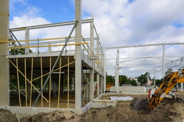 Yeni bir modern fabrikanın inşaat sahası beton ve metal yapı iskeletini güçlendirdi, kazıcılı toprak çalışmaları, kazma kazma kazıları