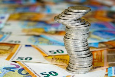 Avro banknotlarının arkaplanındaki iki avroluk dengesiz piramit, durgun ekonomi kavramı, istikrarsız madeni paralar yığını, gelecekteki istikrarsızlık