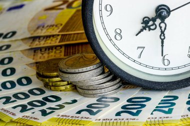Analog masa saatinin bir parçası Avro banknotları ve madeni paralar yığınının üzerinde duruyor, iş konsepti. Zaman paradır, yatırım zamanıdır ve zaman geçer.