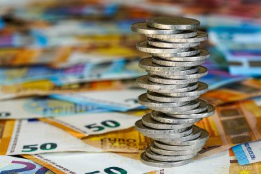 Avro banknotlarının arkaplanındaki iki avroluk dengesiz piramit, durgun ekonomi kavramı, istikrarsız madeni paralar yığını, gelecekteki istikrarsızlık