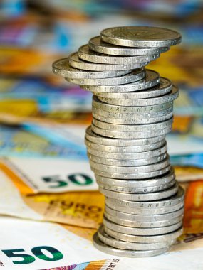Avro banknotlarının arkaplanındaki iki avroluk dengesiz piramit, durgun ekonomi kavramı, istikrarsız madeni paralar yığını, gelecekteki istikrarsızlık