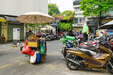 Ho Chi Minh City, Vietnam - 16 Mart 2025: Tüm malzeme ve ekipmanlarla birlikte bir motosikletli sokak satıcısı, Saigon şehir merkezi işlek sokak manzarası
