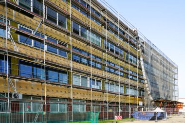 İnşaat çalışmaları, inşaat atıkları boruları ve atık konteynırları sırasında yapı iskelesi ve koruyucu ağla kaplı ofis binasının yenilenmesi