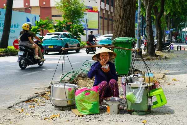 Ho Chi Minh Şehri, Vietnam- 16 Mart 2025: Vietnamlı sokak satıcısı şehir kaldırımında oturuyor, satıştan sonra hızlı bir yemek yiyor.