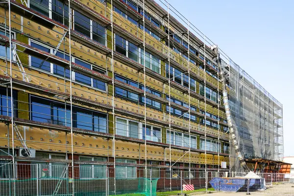 İnşaat çalışmaları, inşaat atıkları boruları ve atık konteynırları sırasında yapı iskelesi ve koruyucu ağla kaplı ofis binasının yenilenmesi