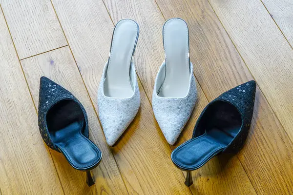 İki çift şık yüksek topuklu katır, beyaz ve siyah parıltılı ayakkabılar ahşap bir zemine dizilmiş şık ve modaya uygun olarak.