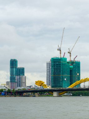 Vietnam, Da Nang 'daki Ejderha Köprüsü' nde altın ejderha heykeli. Uzakta inşaat vinçleri ve modern ufuk çizgisi var.