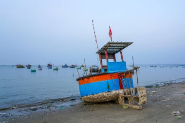 Vietnam 'ın kıyı balıkçı köyünde sakin denizde yüzen yıpranmış pervaneli ve uzak filolu geleneksel sepetli balıkçı teknesi kıyıya vurdu.
