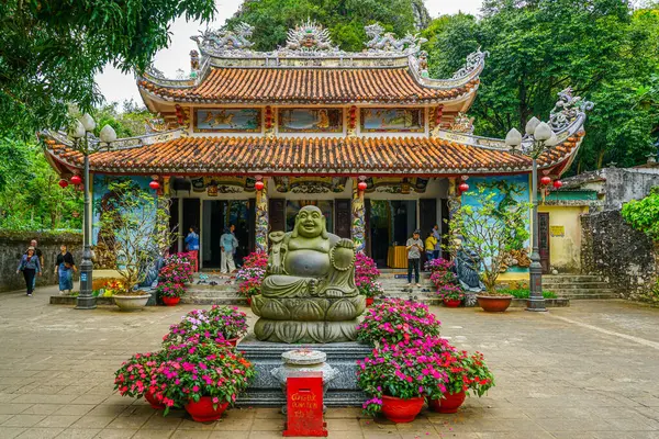 Da Nang, Vietnam- 18 Mart 2025: Çiçek aranjmanları ve ziyaretçileri olan süslü bir Vietnam tapınağının girişinde neşeli Buda heykeli