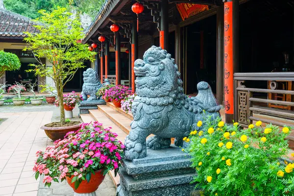 Geleneksel Vietnam tapınağı avlusunun önünde çiçek açan ve kırmızı fenerli taş koruyucu aslan heykelleri.