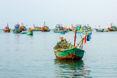 Uzakta düzinelerce parlak Vietnamlı balıkçı teknesiyle ön planda demirlemiş bir ahşap balıkçı teknesi, Mui Ne