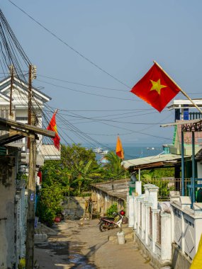 Vietnam 'ın dar sokakları kırmızı bayraklar, motorsikletler, elektrik hatları ve okyanus manzarasına uzanan tropikal yeşilliklerle süslenmiş, Mui Ne