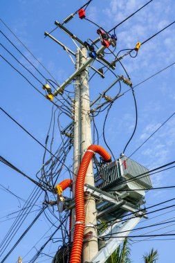 Kaotik elektrik kabloları, trafo ve açık gökyüzü altında parlak turuncu kablolar olan beton elektrik direğine yakın çekim.