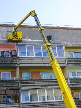 Hidrolik asansörde inşaat işçisi. Üst kattaki apartman bloğunun bakımını yapıyor.