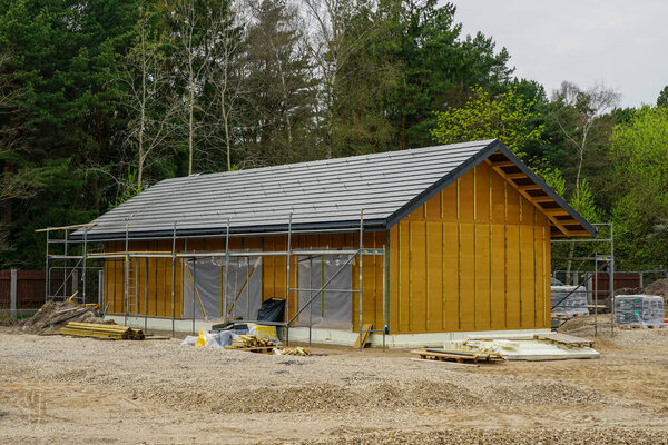 Modern Wooden House Under Construction Near Forest, Sustainable Architecture in Progress with Scaffolding, Roofing, and Building Materials on Site