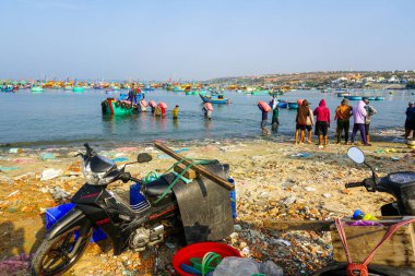 Mui Ne, Vietnam- 22 Mart 2025 İşçilerin ağır erzak torbalarını ve scooterları kirli deniz kıyısına yüklediği kalabalık balıkçı limanı