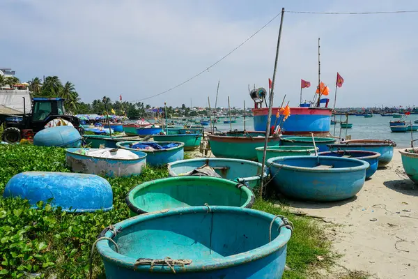 Arka planda balıkçı bayrakları ve kıyı köyü olan kumlu bir sahildeki yuvarlak sepet teknelerin renkli bir koleksiyonu, Mui Ne, Vietnam