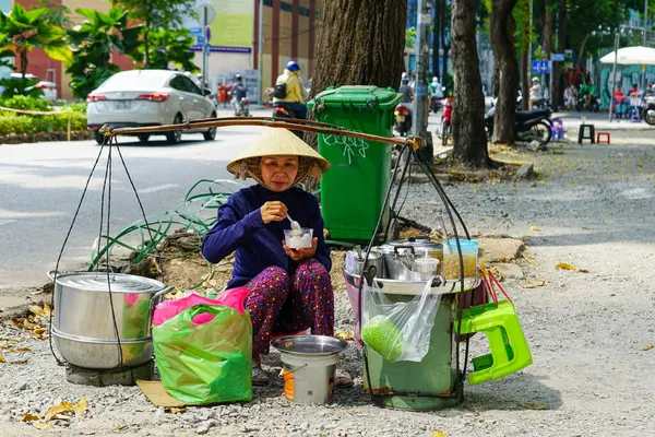 Ho Chi Minh Şehri, Vietnam- 16 Mart 2025: Vietnamlı sokak satıcısı şehir kaldırımında oturuyor, satıştan sonra hızlı bir yemek yiyor.