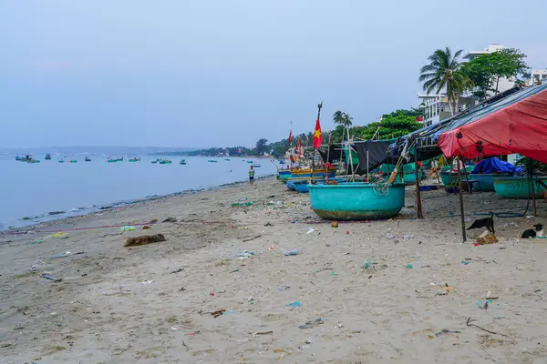 Geleneksel yuvarlak tekneleri, geçici çadırları ve kumlara saçılmış molozları olan huzurlu bir Vietnam kıyısı, Mui Ne balıkçı köyü.