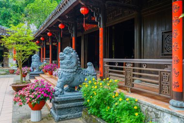 Huzurlu tapınak girişi oyulmuş taş koruyucu aslanlar, kırmızı sütunlar, Çin fenerleri ve yemyeşil çiçeklerle süslenmiş.