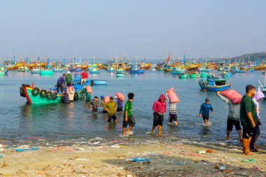 Mui Ne, Vietnam- 22 Mart 2025: İşçiler Vietnam 'da denizcilik faaliyetleriyle dolu bir balıkçı limanında teknelere ağır çuvallar taşıyorlar
