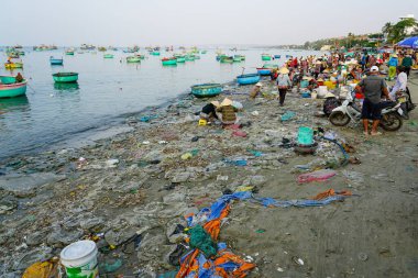 Mui Ne, Vietnam- 22 Mart 2025: Vietnam 'ın kirletilmiş sahillerindeki yerel deniz ürünleri pazarı, balıkçı tekneleri demirlemiş ve insanlar kıyıda taze balık satıyorlar