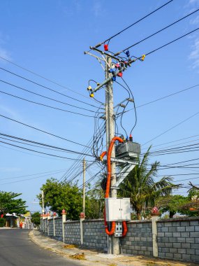 Transformatörlü elektrik direği, karmaşık kablolar, turuncu kanal boruları ve Vietnam caddesinde renkli yalıtıcılar.