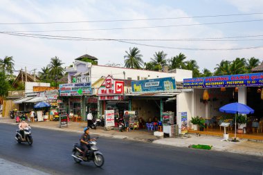 Mui Ne, Vietnam- 21 Mart 2025: Mui Ne 'de hayat dolu bir yol kenarı sahnesi, yerli ve turistlerin canlı dükkanlardan, bir minimart ve scooterlarla yemek yediklerini gösteriyor.