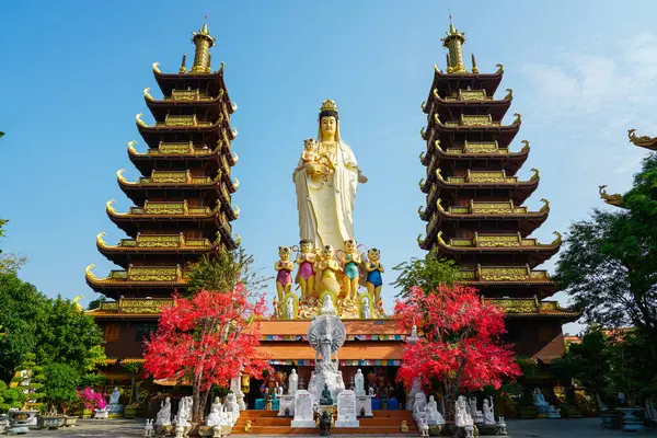 Mui Ne, Vietnam 'daki canlı bir Budist tapınağındaki kırmızı ağaçların üzerinde yükselen iki süslü pagoda tarafından çevrelenmiş Quan Am heykeli.