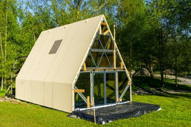 Eksik bir A-çerçeve glamping kabin cam cephe ve açıkta çerçeve, güneşli bir açıklık, nihai montaj bekliyor ve ayrıntılı