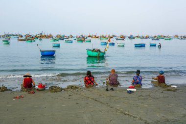 Mui Ne, Vietnam- 22 Mart 2025: Bir grup yerli kadın, sakin sularda yüzen balıkçı teknelerinin deniz manzarasının tadını çıkarıyorlar.
