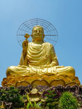 Nilüfer ağacına oturmuş muhteşem bir Buda heykeli açık mavi gökyüzünün altında parıldıyor. Dalat, Vietnam 'da sakin bir bahçede.