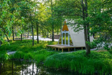 Konforlu, bej kapaklı bir kulübe sakin bir orman göletinin yanındaki ahşap bir platformda duruyor. Doğa aşıkları için mükemmel.