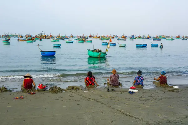 Mui Ne, Vietnam- 22 Mart 2025: Bir grup yerli kadın, sakin sularda yüzen balıkçı teknelerinin deniz manzarasının tadını çıkarıyorlar.