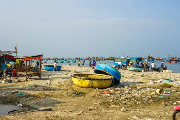 Mui Ne, Vietnam- 22 Mart 2025: Balıkçı tekneleri sahile saçılmış görünür atıklar arasında kalabalık olarak yerel halk ve satıcılar