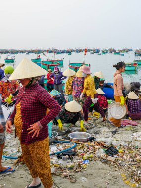 Mui Ne, Vietnam- 22 Mart 2025 Şafak vakti balıkçı kadınlar, teknelerin denize doluştuğu kalabalık bir kıyı şeridi boyunca deniz mahsullerini işlerler.