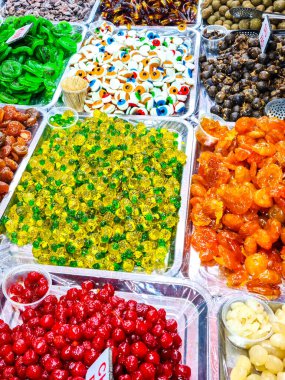 Metal tepsilerde çeşitli şekillerde, renklerde ve dokularda çeşitli meyveler, jelibonlar ve çiğnenmiş tatlılar sergileniyor.