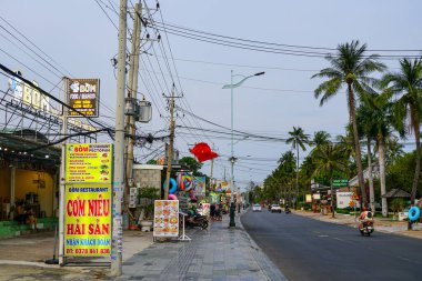 Mui Ne, Vietnam- 20 Mart 2025: Canlı bir sokak sahnesi Nguyen Dinh Chieu Caddesi boyunca Bom Restoranı, elektrik hatları, palmiye ağaçları ve dükkanları gösteriyor
