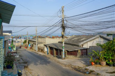 Mui Ne, Vietnam-March22, 2025: Mui Ne 'de sakin bir yol, yoğun, karmaşık elektrik hatları ve mütevazı kıyı evleri tarafından çerçevelenen hareketli bir balıkçı limanına çıkar.