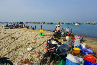 Mui Ne, Vietnam- 22 Mart 2025: Satıcıların sepet hazırladığı canlı bir balıkçılık sahnesi ve yerel halk dağınık, kumlu bir sahil boyunca balıkçı teknelerinin yanında toplanıyor.