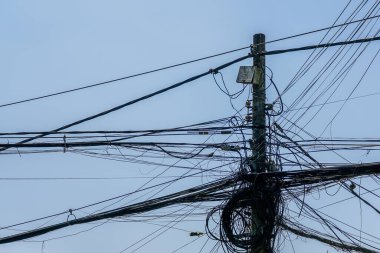 Bir elektrik direğine bağlı karmaşık kablo ve kablolardan oluşan yoğun bir küme kaotik şehir altyapısını vurguluyor.