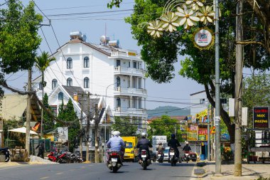 Da Lat, Vietnam- 24 Mart 2025: Motosikletliler Da Lat 'ta hareketli bir cadde boyunca binalar, tabelalar ve birbirine dolanmış tellerle dolaşıyorlar.