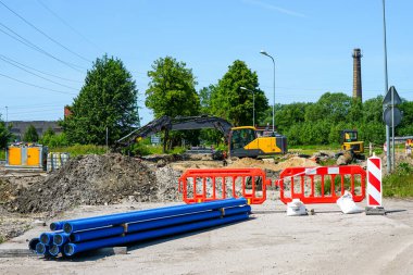 Mavi borular ve güvenlik bariyerleri, kazıcıların faaliyet halinde olduğu bir inşaat alanının önünü işaret ediyor