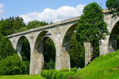 Polonya 'daki ikonik Stanczyki Köprüsü parlak mavi gökyüzünün altındaki yeşil bir ormanda bulunan heybetli taş kemerlerle dimdik ayakta duruyor.