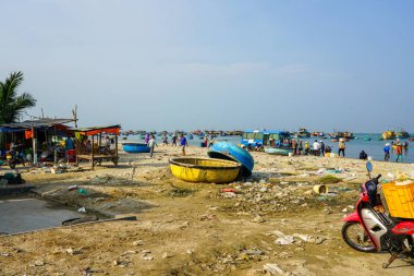 Mui Ne, Vietnam- 22 Mart 2025: Yerel halk kıyıda balıkçı tekneleri ve satıcıların yanında toplanıyor, tekneler, motorsikletler ve çöpler denizle buluşuyor.
