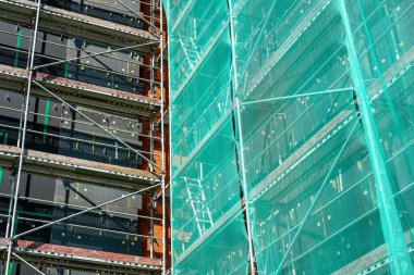 Tadilat altındaki bir binada açık iskele, yalıtım panelleri ve işçi güvenliği için koruyucu yeşil ağlar görülüyor.