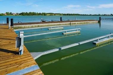 Sakin bir göle demirlemiş temiz metal kayıkla modern ahşap rıhtım. Tekne, yelken ve deniz kenarında dinlenmek için ideal bir yer.