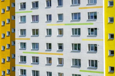 Parlak sarı panelleri ve pencereli beyaz duvarları olan yüksek katlı bir apartman cephesinin yakın görüntüsü